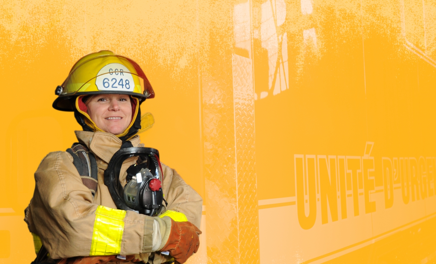Smiling firefighter wearing helmet and safety gear. Their arms are crossed.