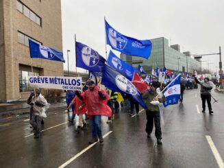 Image: A group of unionists with flags march down a street in rainy, cold weather.